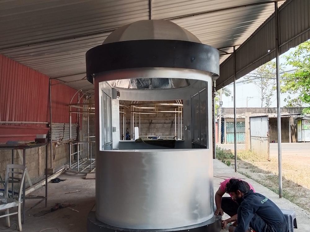 A round kiosk with a domed roof being assembled in the workshop, with a fabricator fixing the base trim